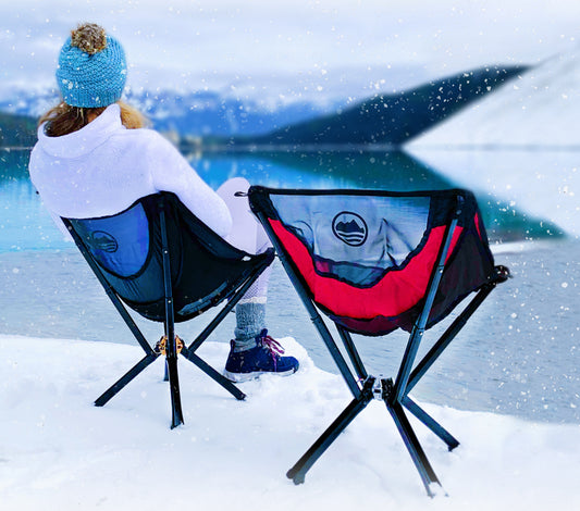 Woman sitting in cliq chair next to empty cliq chair, on a bed of snow overlooking a winter scene