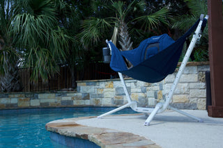 Blue Kammok Perch hammock chair with a cup holder on a white stand beside a pool