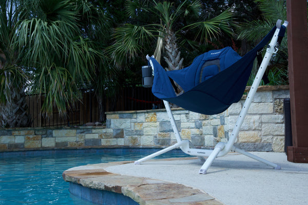 Blue perch hammock chair on a stand by a pool with palm trees in the background