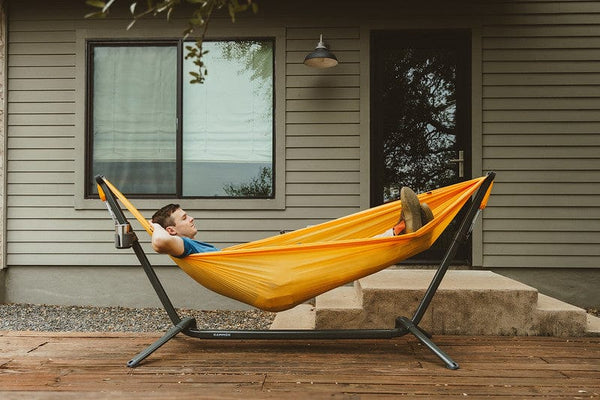 Person relaxing in a yellow hammock in the swiftlet hammock stand on a stand outside a house.