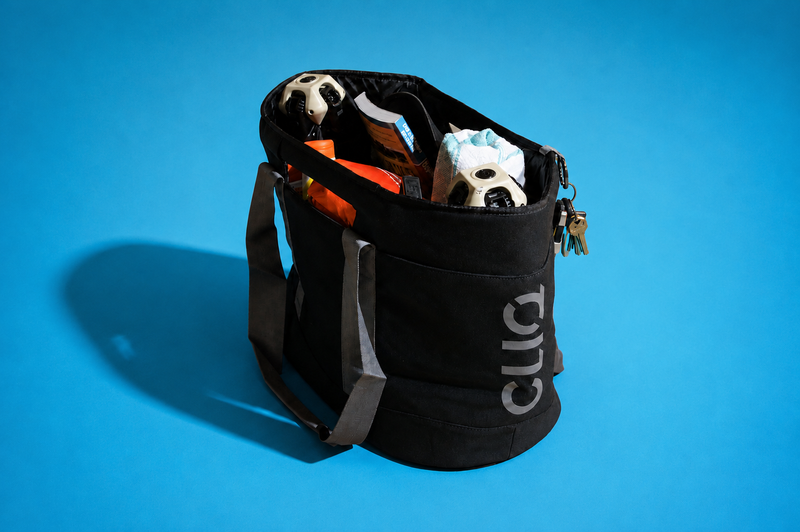 A black ToQ tote bag with gray handles, shown open with various items inside, including soccer balls, on a solid blue background.