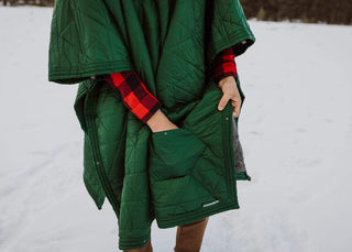 Person wearing a green Kammok Mountain Blanket as a poncho in the snow