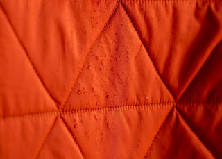 Water beading on the quilted shell of the Ember Orange Mountain Blanket