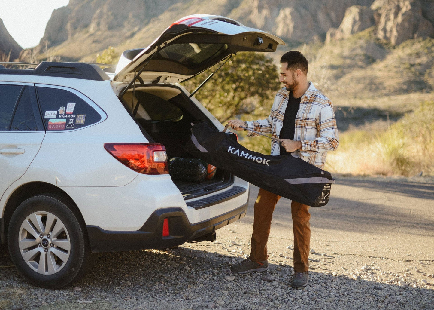 Man loading a Kammok hammock swiftlet stand into the trunk of a car in a desert setting