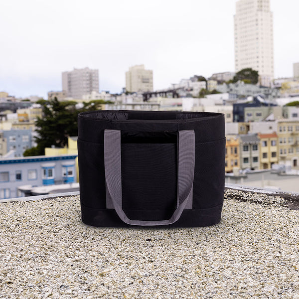 Black tote bag with gray handles on a rooftop with cityscape in the background