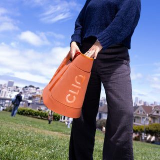 Person holding an orange bag with 'CLIQ' branding outdoors on a sunny day - ToQ Bag Orange