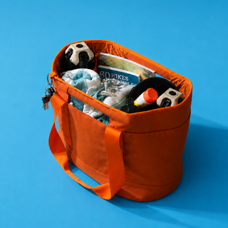 An orange canvas organizer ToQ tote bag filled with various items, including a soccer ball, CLIQ ClassiQ Chairs, and a magazine, set against a solid blue background.